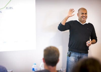 Smiling presenter waving to audience during a business workshop with growth chart projected on screen