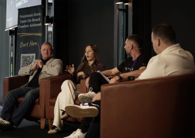 Panel discussion at SYSTEMology Summit 2023 with four speakers seated in leather chairs on stage